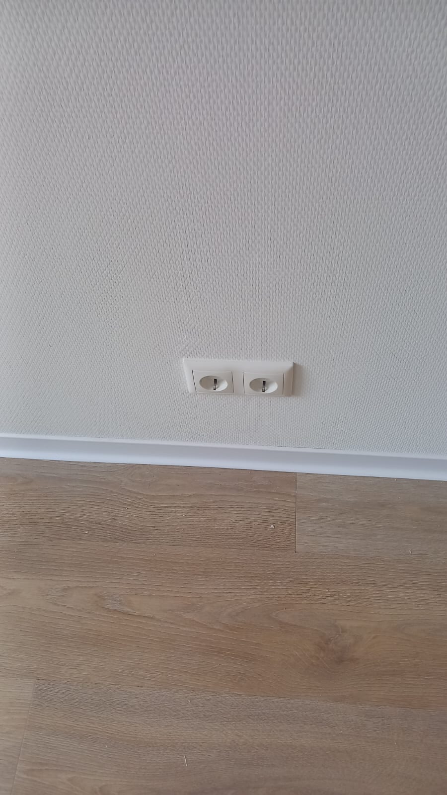 Afgewerkte wand met dubbele wandcontactdoos en houten vloer